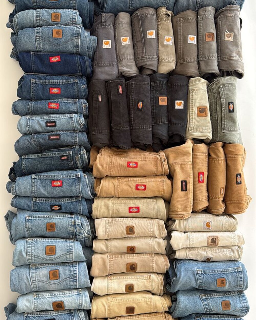 Dozens of folded vintage Carhartt and Dickies pants sorted into colour-graded stacks